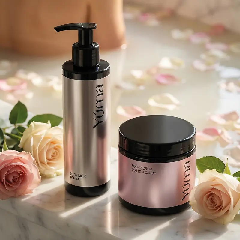 Προϊόντα Body Care της YUMA δίπλα σε τριαντάφυλλα, με φόντο μπανιέρα γεμάτη ροδοπέταλα.