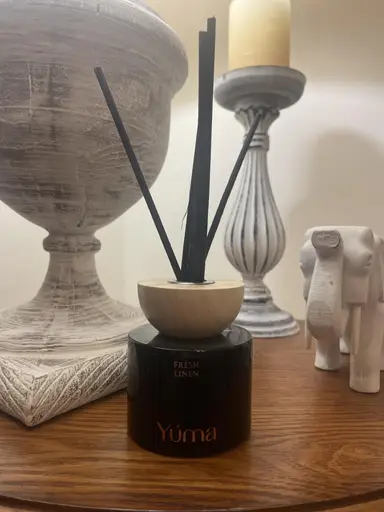 Μαύρο αρωματικό χώρου Fresh Linen της YUMA με ξύλινο καπάκι και μαύρα στικ σε ξύλινη επιφάνεια.