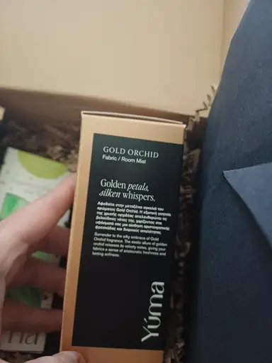 Χάρτινη συσκευασία Fabric Room Mist Gold Orchid της YUMA μέσα σε κουτί με προστατευτικό χαρτί.