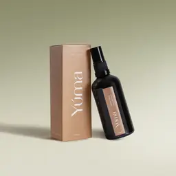 Σκούρο γυάλινο μπουκάλι Pine Tree Fabric Mist της YUMA δίπλα στην μπεζ χάρτινη συσκευασία του.