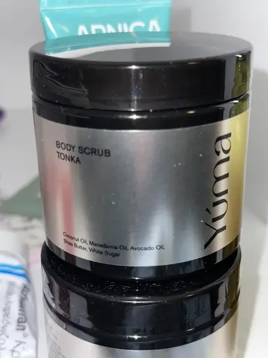 Μεταλλικό βάζο Body Scrub Tonka της YUMA με μαύρο καπάκι πάνω σε παρόμοια συσκευασία.
