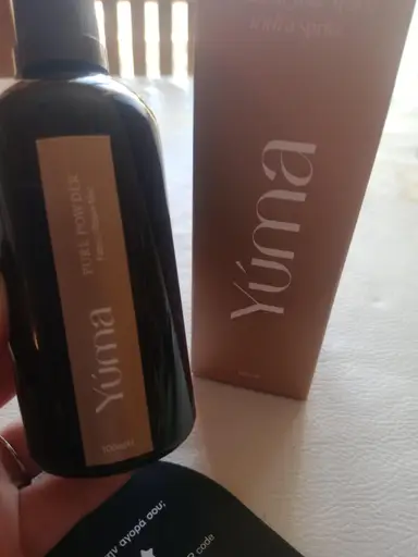 Σκούρο γυάλινο μπουκάλι Pure Powder της YUMA δίπλα στη χάρτινη συσκευασία του σε μπεζ φόντο.