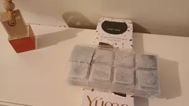 Γκρι wax melts σε σχήμα κύβου μέσα σε πλαστική συσκευασία πάνω σε λευκό κουτί της YUMA.