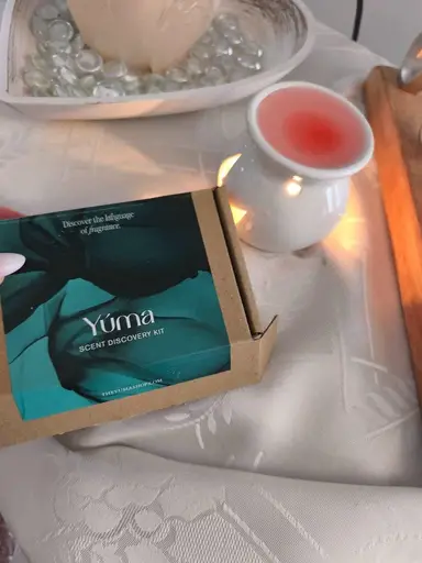 Κουτί SCENT DISCOVERY KIT της Yúma δίπλα σε αναμμένο λευκό καυστήρα με ροζ λιωμένο κερί.