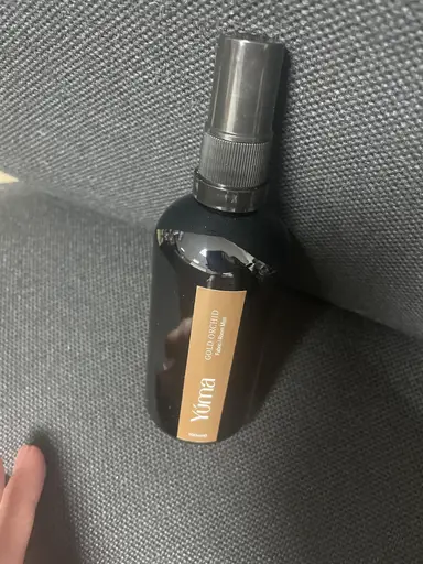 Μαύρο μπουκάλι Room Mist της YUMA με άρωμα Gold Orchid πάνω σε γκρι υφασμάτινη επιφάνεια.