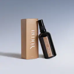Σκούρο γυάλινο μπουκάλι Fresh Linen Fabric/Room Mist δίπλα στη μπεζ χάρτινη συσκευασία της YUMA, σε γαλάζιο φόντο.