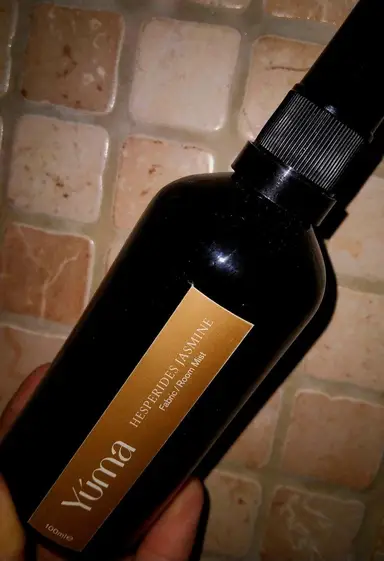 Σκούρο μπουκάλι Room Mist της YUMA με χρυσή ετικέτα Hesperides Jasmine πάνω σε πέτρινη επιφάνεια.