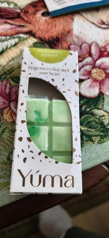 Πράσινο wax melt σε λευκή συσκευασία της YUMA με το άρωμα Hesperides Jasmine πάνω σε υφασμάτινη επιφάνεια.