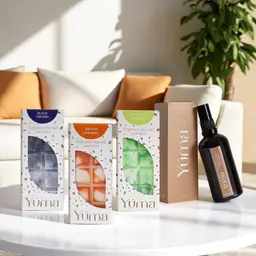 Τρία wax melts YUMA και ένα room spray Eternal Eden σε λευκό τραπέζι μπροστά από καναπέ.
