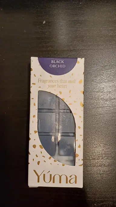 Μπλε wax melt Black Orchid της YUMA σε λευκή συσκευασία με χρυσές λεπτομέρειες πάνω σε σκούρα επιφάνεια.