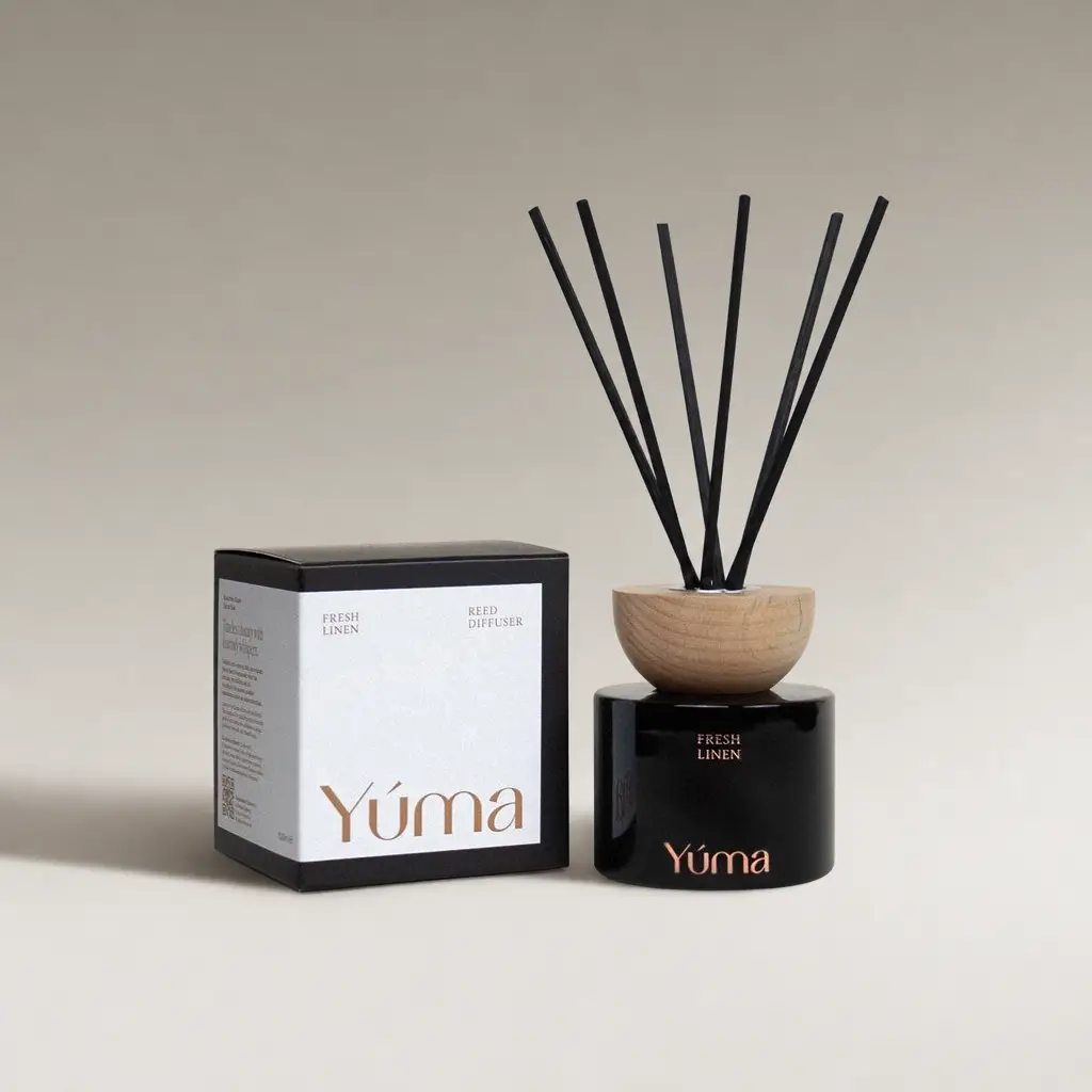 Μαύρο γυάλινο Reed Diffuser Fresh Linen της YUMA με ξύλινο καπάκι δίπλα στη χάρτινη συσκευασία του.