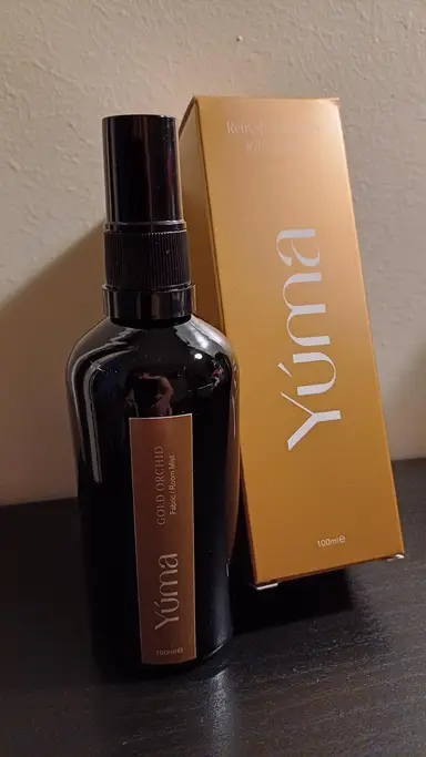 Μαύρο μπουκάλι Room Mist Gold Orchid της YUMA δίπλα στη χρυσή συσκευασία του.