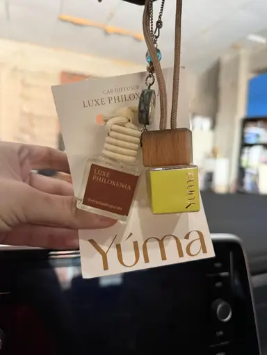 Δύο μικρά γυάλινα αρωματικά αυτοκινήτου YUMA με ξύλινα πώματα κρεμασμένα μπροστά από λευκή κάρτα.