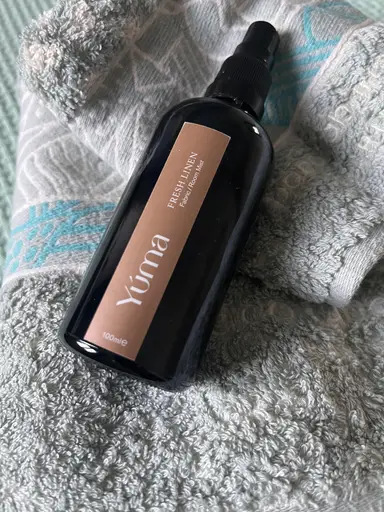 Μαύρο μπουκάλι Fresh Linen Fabric Room Mist της YUMA τοποθετημένο πάνω σε γκρίζα βαμβακερή πετσέτα.