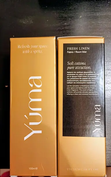 Δύο χρυσές συσκευασίες Fresh Linen Fabric Room Mist της YUMA σε μαύρο φόντο.