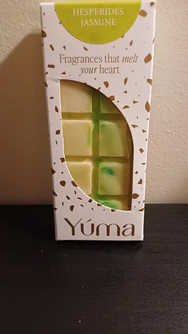 Λευκή συσκευασία YUMA Hesperides Jasmine με κερί σε σχήμα σοκολάτας με πράσινες και κίτρινες αποχρώσεις.