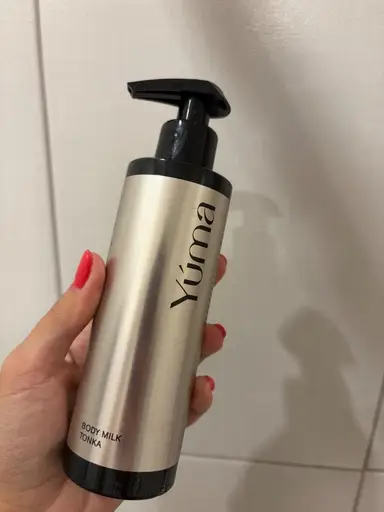Ένα χέρι κρατά το Body Milk Tonka της YUMA σε μεταλλικό μπουκάλι με μαύρη αντλία.