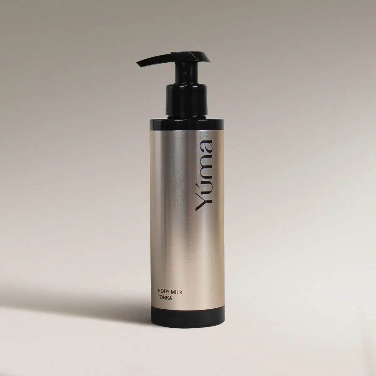 Μεταλλικό μπουκάλι Body Milk Tonka της YUMA με μαύρη αντλία σε ουδέτερο φόντο.