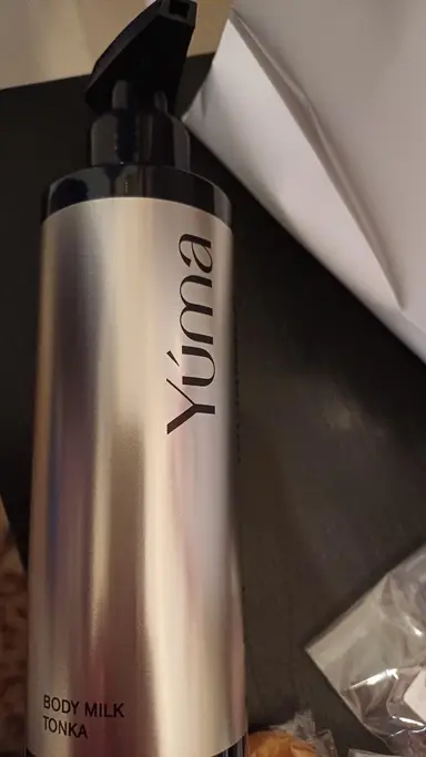 Μεταλλικό μπουκάλι Body Milk Tonka της YUMA με μαύρη αντλία πάνω σε σκούρα επιφάνεια.