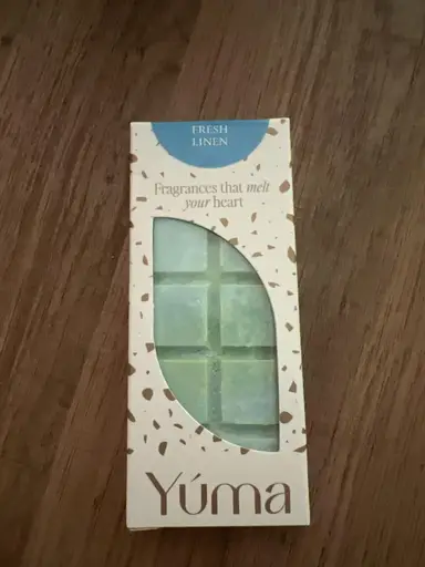 Συσκευασία wax melt της YUMA σε άρωμα Fresh Linen με γαλάζιους κύβους κεριού σε ξύλινη επιφάνεια.