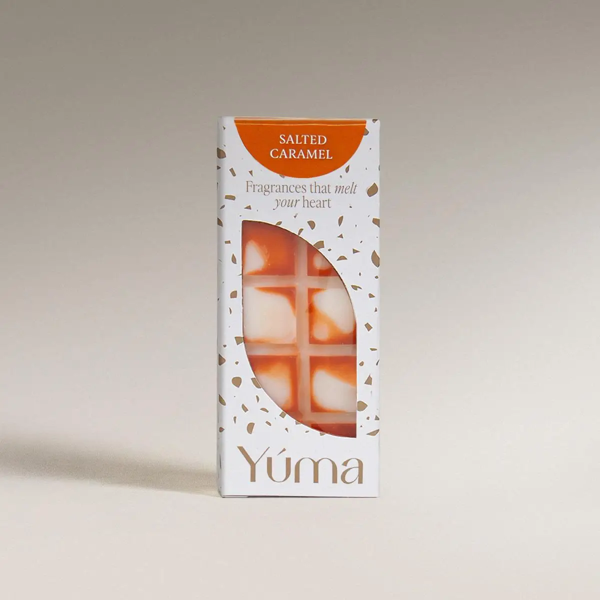 Λευκή συσκευασία wax melts Salted Caramel της YUMA με πορτοκαλί λεπτομέρειες σε ουδέτερο φόντο.