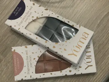 Δύο συσκευασίες wax melts της YUMA με αρώματα Black Orchid και Gingerbread Cookies σε ξύλινη επιφάνεια.