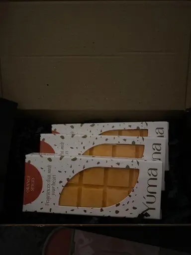 Τρεις συσκευασίες Orange Spices wax melts της YUMA τοποθετημένες μέσα σε κουτί με μαύρο προστατευτικό χαρτί.