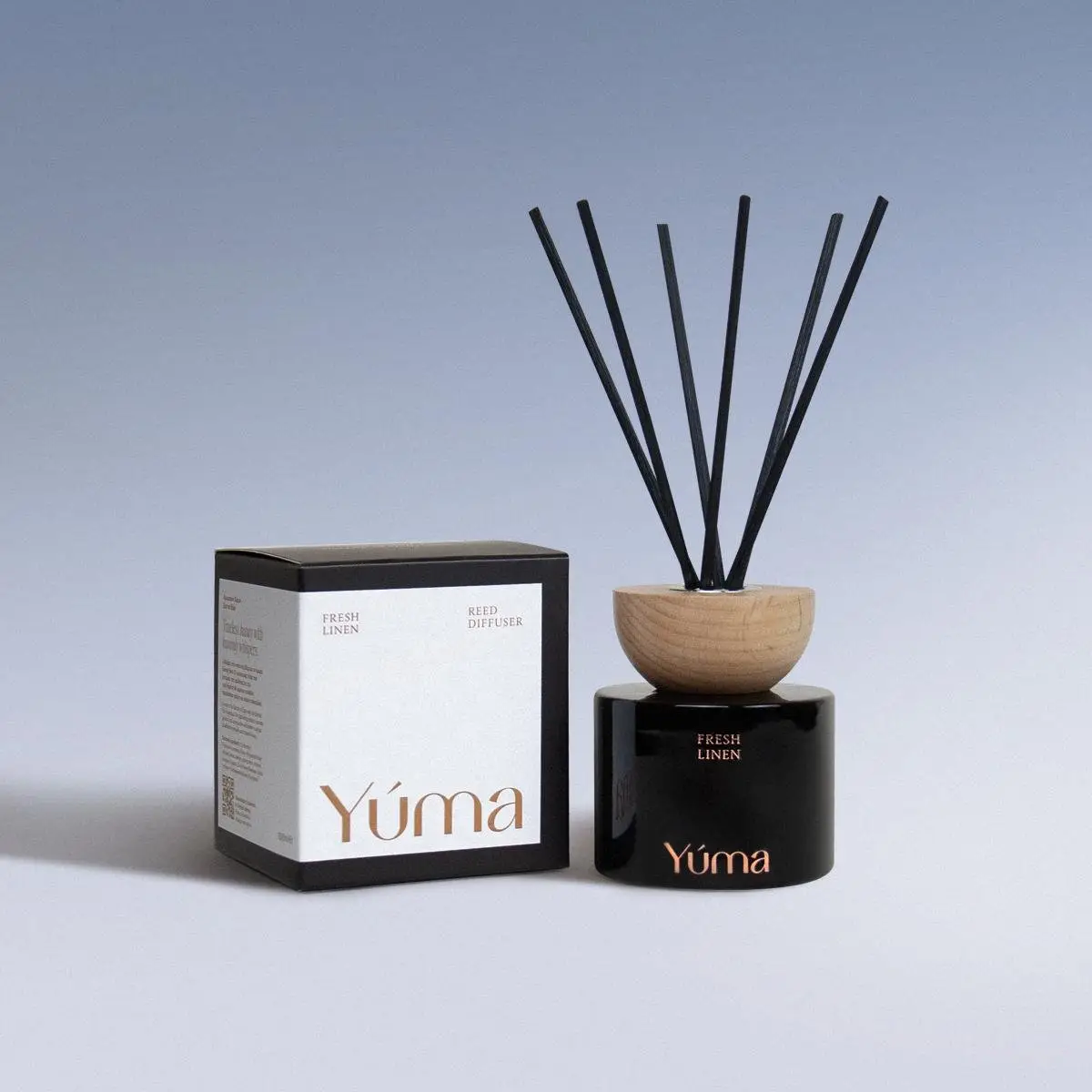 Μαύρο γυάλινο Reed Diffuser Fresh Linen της YUMA με ξύλινο καπάκι δίπλα στη χάρτινη συσκευασία του.