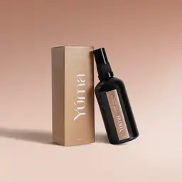 Μαύρο μπουκάλι Fabric Mist Amber Tobacco της YUMA δίπλα στο μπεζ κουτί του σε ομοιόμορφο φόντο.