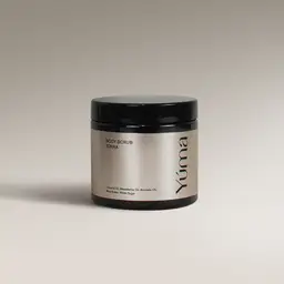 Μαύρο βάζο Body Scrub της YUMA με άρωμα Tonka και ασημί ετικέτα σε γκρίζο φόντο.