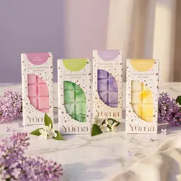 Τέσσερα wax melts της YUMA σε χάρτινες συσκευασίες πάνω σε μάρμαρο με άνθη πασχαλιάς και γιασεμιού.