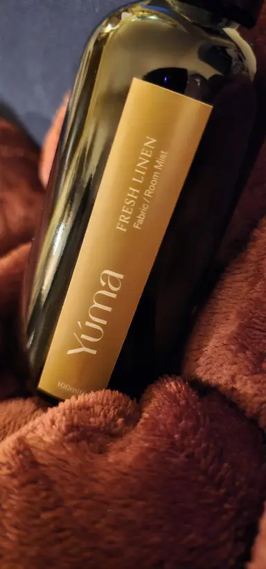 Σκούρο γυάλινο μπουκάλι Fresh Linen της YUMA τοποθετημένο πάνω σε μαλακό καφέ ύφασμα.
