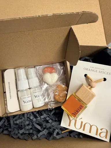 Ανοιχτό κουτί της YUMA με αρωματικά σπρέι, wax melts σε σχήμα καρδιάς και ένα αρωματικό αυτοκινήτου Orange Spices.