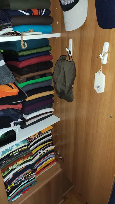 Αρωματικό κερί ντουλάπας κρεμασμένο σε ξύλινη επιφάνεια δίπλα σε στοίβες με πολύχρωμα διπλωμένα ρούχα.