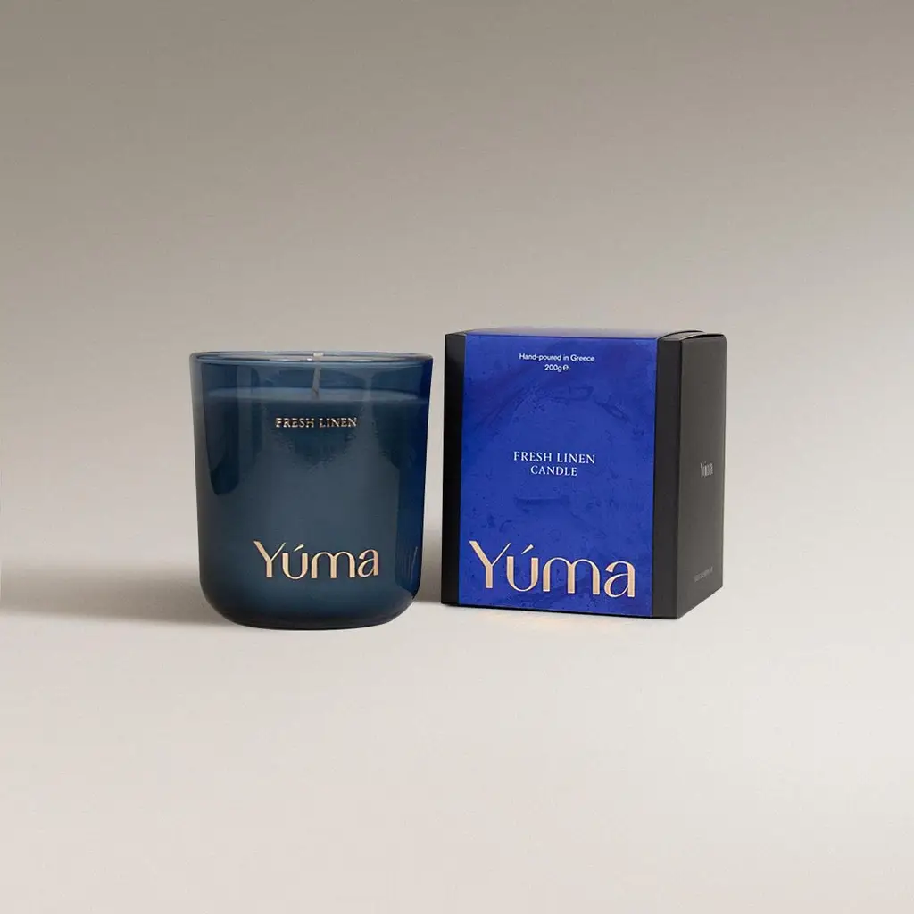 Αρωματικό κερί Fresh Linen της YUMA σε μπλε γυάλινο δοχείο δίπλα στη χάρτινη συσκευασία του.