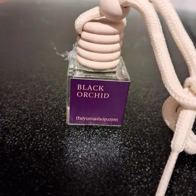 Μικρό γυάλινο αρωματικό αυτοκινήτου Black Orchid με ξύλινο πώμα και μπεζ σχοινί σε μαύρη επιφάνεια.