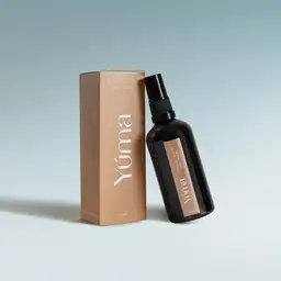 Σκούρο γυάλινο μπουκάλι spray Cycladic Roots της YUMA δίπλα στην μπεζ χάρτινη συσκευασία του.