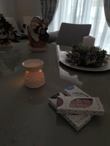 Συσκευασίες wax melts YUMA δίπλα σε αναμμένο αρωματιστή και χριστουγεννιάτικη διακόσμηση πάνω σε τραπέζι.