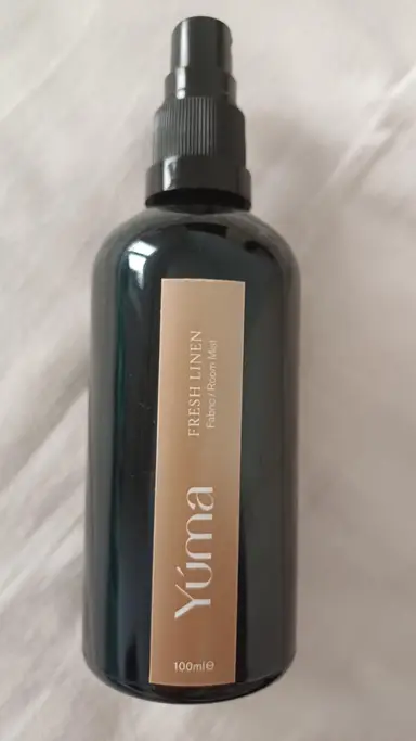 Σκούρο γυάλινο μπουκάλι Room Mist της YUMA με μπεζ ετικέτα Fresh Linen πάνω σε λευκό ύφασμα.