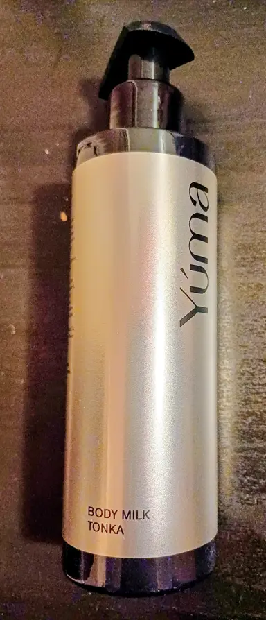 Ένα μπουκάλι Body Milk TONKA της YUMA με μαύρη αντλία σε σκούρο φόντο.