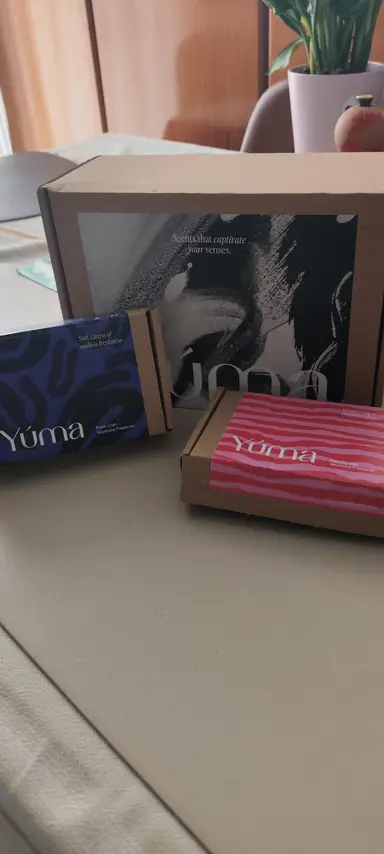 Ένα μεγάλο χάρτινο κουτί YUMA δίπλα σε δύο μικρότερες συσκευασίες με μπλε και ροζ σχέδια.