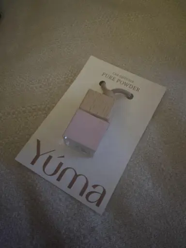 Μικρό γυάλινο αρωματικό αυτοκινήτου Pure Powder της YUMA με ξύλινο πώμα πάνω σε λευκή κάρτα.