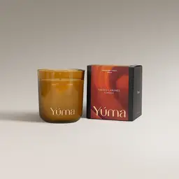 Κερί Salted Caramel της YUMA σε κεχριμπαρένιο γυάλινο δοχείο δίπλα στη χάρτινη συσκευασία του.