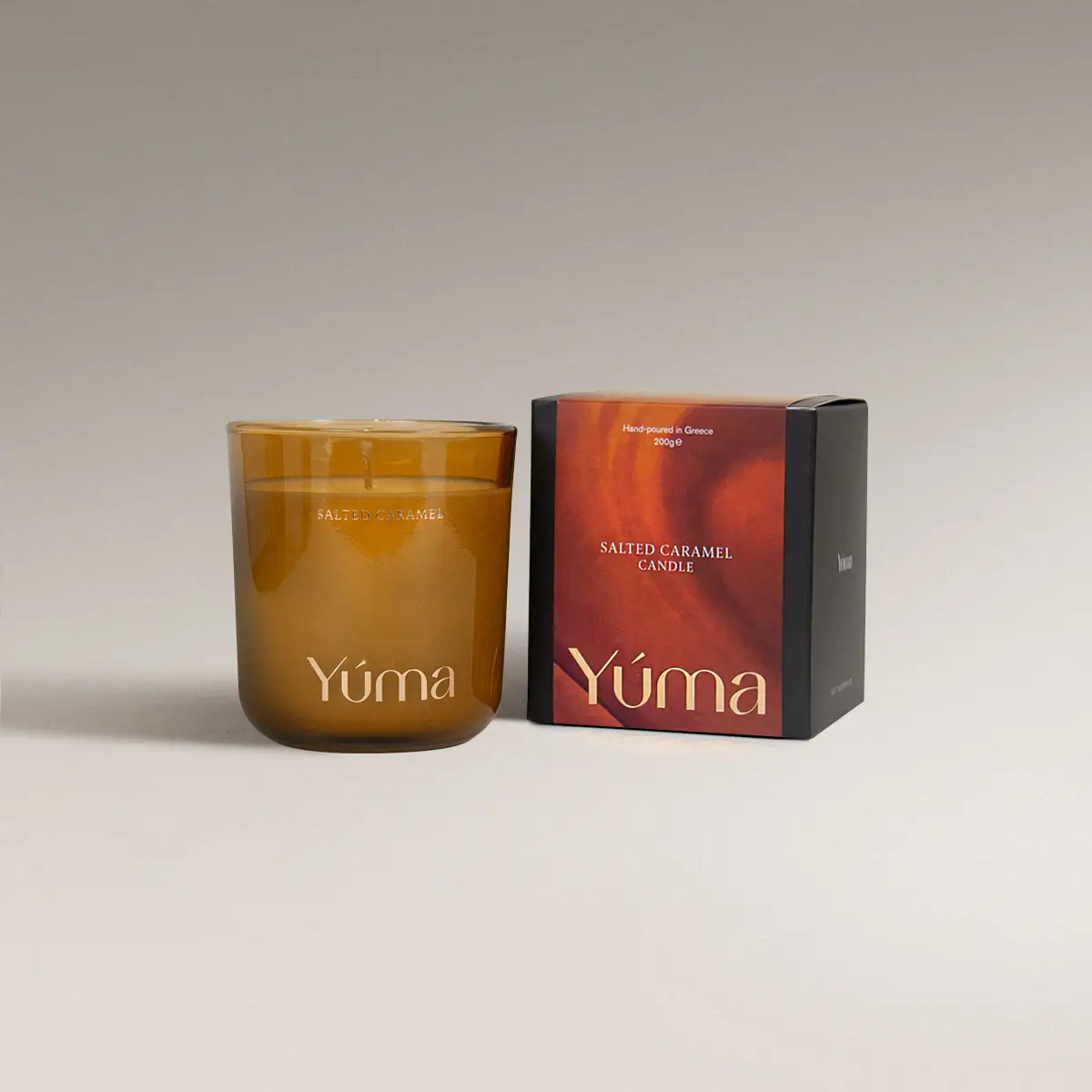 Κερί Salted Caramel της YUMA σε κεχριμπαρένιο γυάλινο δοχείο δίπλα στη χάρτινη συσκευασία του.