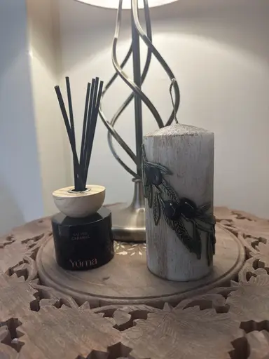 Reed diffuser Salted Caramel της YUMA και διακοσμητικό κερί με σχέδιο ελιάς πάνω σε ξύλινο τραπέζι.
