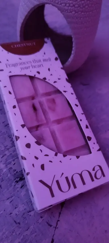 Συσκευασία YUMA με wax melts σε σχήμα σοκολάτας δίπλα σε κεραμικό αρωματιστή υπό μωβ φωτισμό.