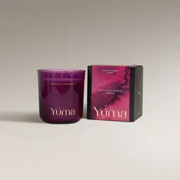 Κερί Apple Cinnamon της YUMA σε καπνιστό ροζ γυάλινο δοχείο δίπλα στη χάρτινη συσκευασία του.