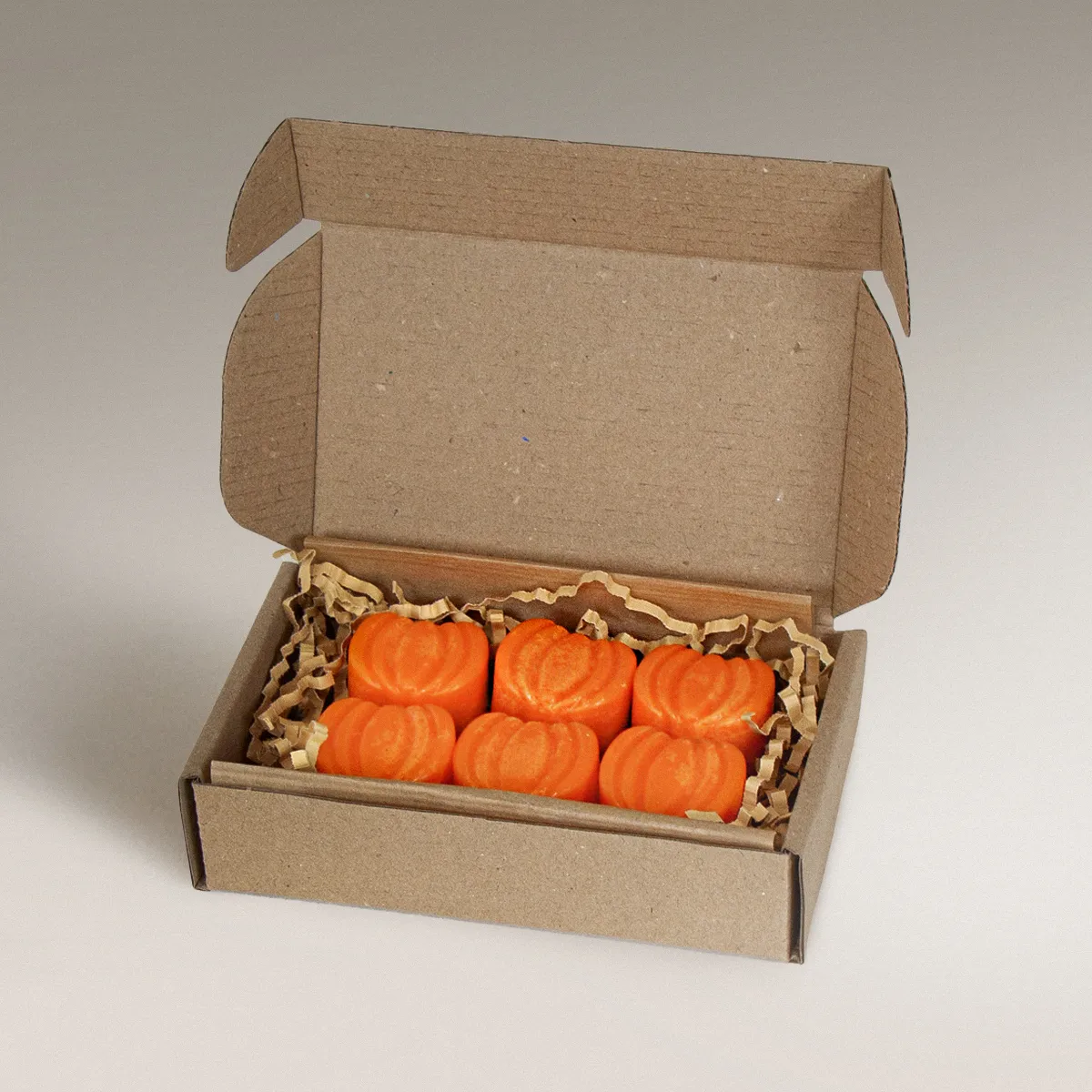 Έξι πορτοκαλί Pumpkin Pie wax melts σε σχήμα κολοκύθας μέσα σε ανοιχτό χάρτινο κουτί συσκευασίας.