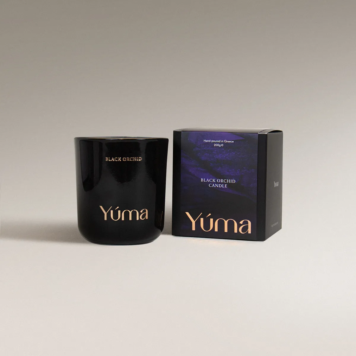 Μαύρο γυάλινο κερί Black Orchid της YUMA δίπλα στη χάρτινη συσκευασία του σε γκρι φόντο.
