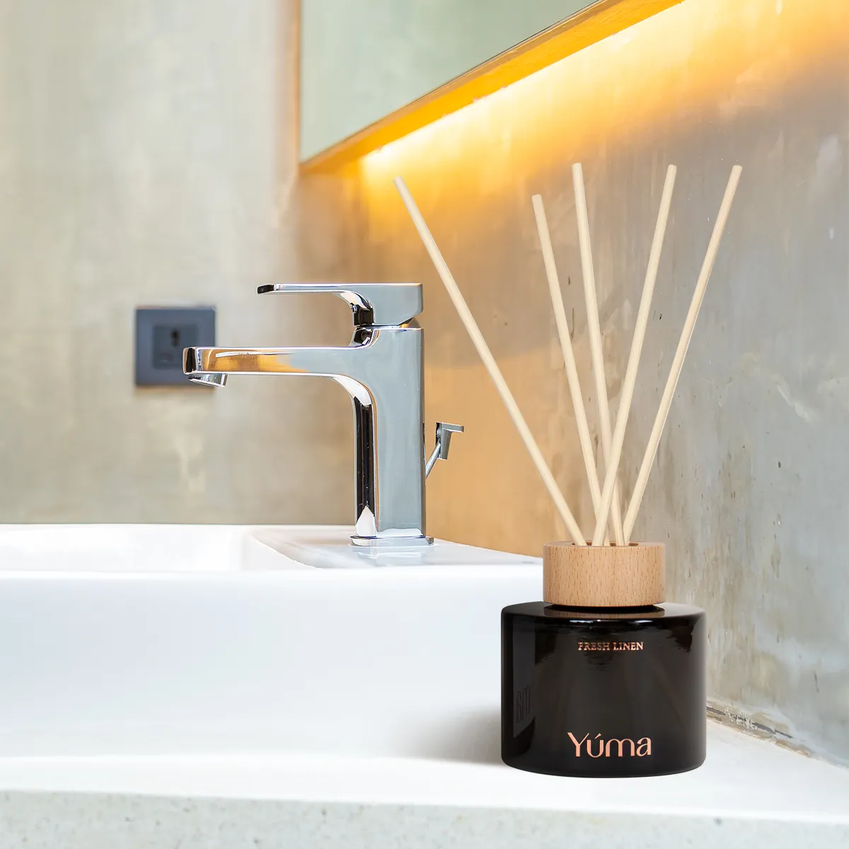 Reed diffuser της YUMA με άρωμα Amber Tobacco σε μαύρο γυάλινο δοχείο δίπλα σε νιπτήρα μπάνιου.